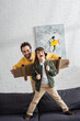 © LIGHTFIELD STUDIOS - Happy man playing with son in aviator costume on couch