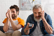 © LIGHTFIELD STUDIOS - Worried man holding remote controller near blurred son on couch