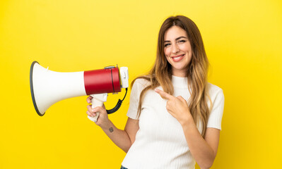 Wall Mural - Caucasian woman isolated on yellow background holding a megaphone and pointing side