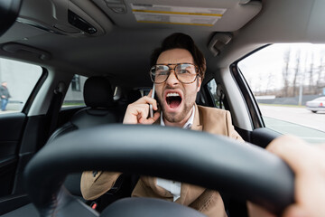 Wall Mural - angry man talking on smartphone while driving car on blurred foreground