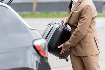 Wall Mural - cropped view of man in suit putting suitcase in car trunk