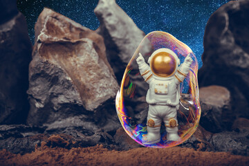 Astronaut raising arms in a soap bubble while standing on rocky mountain. Spaceman wearing white space suit and helmet.