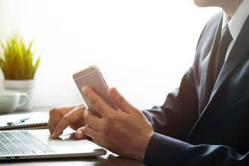 man hand using mobile and typing keyboard of laptop computer on office desk. Workspace, businessman working project creative idea for job online network. Business finance and technology concept.