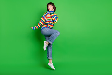 Sticker - Full length photo of impressed cute woman wear sweater jumping high arm cheek looking empty space isolated green color background