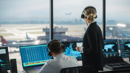 Wall Mural - Female and Male Air Traffic Controllers with Headsets Talk in Airport Tower. Office Room is Full of Desktop Computer Displays with Navigation Screens, Airplane Departure and Arrival Data for the Team.