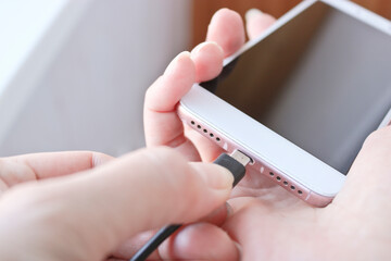 Woman plugging a USB cable into a smartphone connector to charge. Special charging connector for phone.