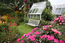 Seat Outside A Victorian Greenhouse Overlooking A Beautiful Cottage Flower Garden