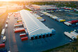 Logistics park with warehouse and loading hub. Semi-trailers trucks stand at ramps and wait for load and unload goods. Aerial view at sunset