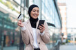 Arabic business woman using phone and holding credit card outdoors