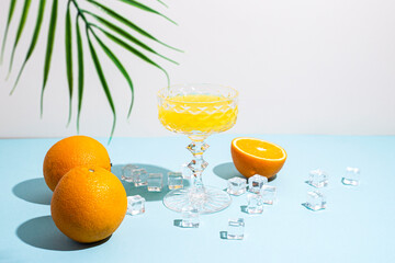 glass with orange juice, oranges, ice cubes, palm leaf on a blue background