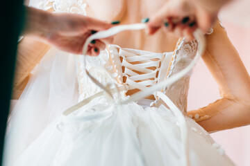 The bridesmaid prepares the bride for the wedding day, helps to button and tie her dress. Bridesmaid makes a bow on the back of the bride's wedding dress, the bride's morning gathering