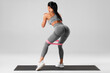 © nikolas_jkd - Athletic girl doing exercise for glute with resistance band on gray background. Fitness woman working out