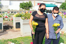 Couple Standing At The Grave Of A Deceased Person In The Cemetery, Wearing A Protective Mask. Death, Graveyard, Loss Of Loved Ones Due To Pandemic.