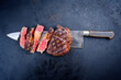Traditional barbecue dry aged wagyu rib-eye beef steaks sliced and served as top view on a rustic large knife on a black board with copy space