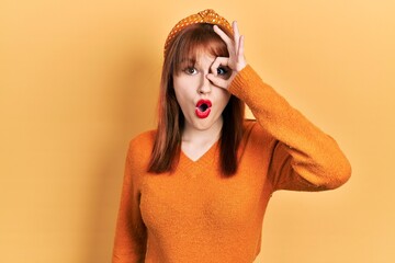 Canvas Print - Redhead young woman wearing casual orange sweater doing ok gesture shocked with surprised face, eye looking through fingers. unbelieving expression.