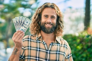 Wall Mural - Young caucasian man smiling happy holding usa dollars at the park.