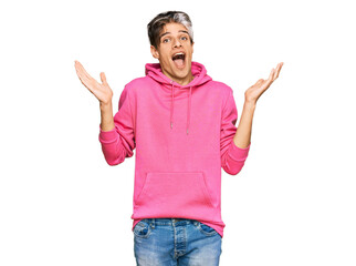 Sticker - Young hispanic man wearing casual pink sweatshirt celebrating crazy and amazed for success with arms raised and open eyes screaming excited. winner concept