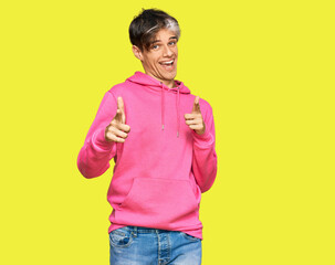 Sticker - Young hispanic man wearing casual pink sweatshirt pointing fingers to camera with happy and funny face. good energy and vibes.