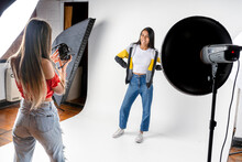 Photo Session Of A Model And A Woman Photographer In A Photography Studio With Flashes And A White Background. Fashion Concept.