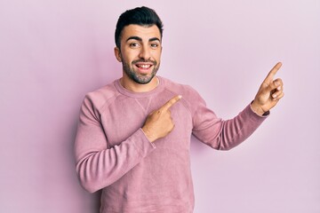 Wall Mural - Young hispanic man wearing casual clothes smiling and looking at the camera pointing with two hands and fingers to the side.