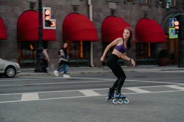 Slim sporty young woman uses rollerskates as mode of transportation in city enjoys favorite hobby ans boosts mood dressed in active wear poses on road exercises regularly keeps fit loses weight