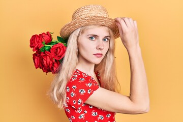 Canvas Print - Beautiful caucasian woman with blond hair holding bouquet of red roses relaxed with serious expression on face. simple and natural looking at the camera.