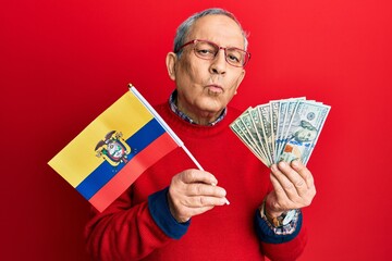 Poster - Handsome senior man with grey hair holding ecuador flag and dollars looking at the camera blowing a kiss being lovely and sexy. love expression.