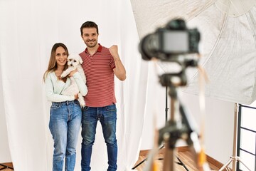 Couple of boyfriend and girlfriend with dog posing as model at photography studio screaming proud, celebrating victory and success very excited with raised arms