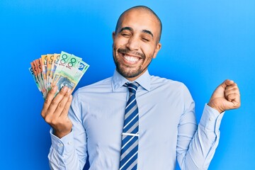 Wall Mural - Hispanic adult man holding australian dollars screaming proud, celebrating victory and success very excited with raised arm