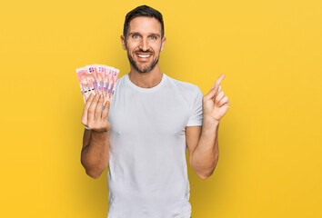 Wall Mural - Handsome man with beard holding south african 50 rand banknotes smiling happy pointing with hand and finger to the side