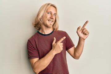 Sticker - Caucasian young man with long hair wearing casual striped t shirt smiling and looking at the camera pointing with two hands and fingers to the side.