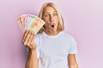 Sticker - Caucasian young man with long hair holding philippine peso banknotes scared and amazed with open mouth for surprise, disbelief face