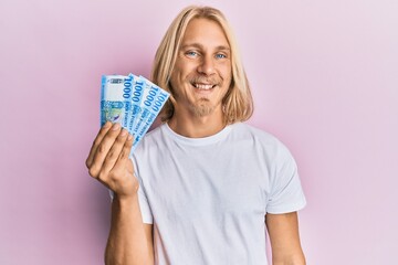 Canvas Print - Caucasian young man with long hair holding 1000 hungarian forint banknotes looking positive and happy standing and smiling with a confident smile showing teeth