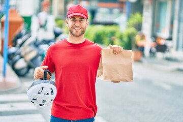 Sticker - Young caucasian deliveryman smiling happy holding delivery paper bag at the city.