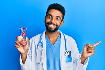 Poster - Handsome hispanic man with beard wearing doctor uniform holding heart smiling happy pointing with hand and finger to the side