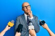 © Krakenimages.com - Bald man with beard being interviewed by reporters holding microphones thinking concentrated about doubt with finger on chin and looking up wondering