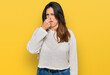 Beautiful hispanic woman wearing casual sweater smelling something stinky and disgusting, intolerable smell, holding breath with fingers on nose. bad smell