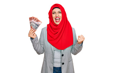 Sticker - Beautiful hispanic woman wearing islamic hijab holding australian dollars banknotes screaming proud, celebrating victory and success very excited with raised arms