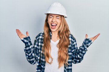 Canvas Print - Young caucasian woman wearing architect hardhat celebrating mad and crazy for success with arms raised and closed eyes screaming excited. winner concept