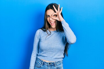 Young brunette teenager wearing casual sweater doing ok gesture with hand smiling, eye looking through fingers with happy face.