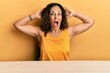 Beautiful middle age woman wearing casual clothes sitting on the table crazy and scared with hands on head, afraid and surprised of shock with open mouth
