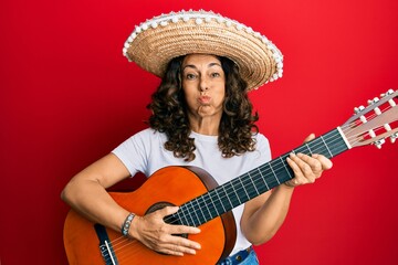 Sticker - Middle age hispanic woman holding mexican hat playing classical guitar puffing cheeks with funny face. mouth inflated with air, catching air.