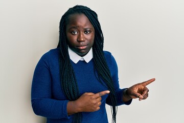 Poster - Young black woman with braids pointing up with fingers to the side skeptic and nervous, frowning upset because of problem. negative person.