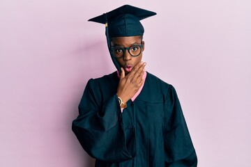 Sticker - Young african american girl wearing graduation cap and ceremony robe looking fascinated with disbelief, surprise and amazed expression with hands on chin