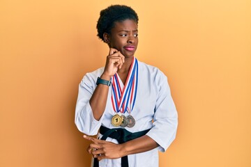 Wall Mural - Young african american girl wearing karate kimono and black belt serious face thinking about question with hand on chin, thoughtful about confusing idea