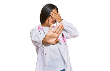 Canvas Print - Beautiful hispanic woman wearing doctor uniform and stethoscope covering eyes with hands and doing stop gesture with sad and fear expression. embarrassed and negative concept.