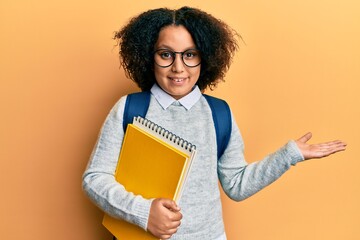 Sticker - Young little girl with afro hair wearing school bag and holding books celebrating achievement with happy smile and winner expression with raised hand