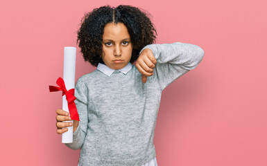 Sticker - Young little girl with afro hair holding graduate degree diploma with angry face, negative sign showing dislike with thumbs down, rejection concept