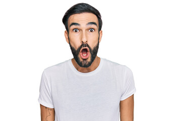 Wall Mural - Young hispanic man wearing casual white t shirt afraid and shocked with surprise expression, fear and excited face.