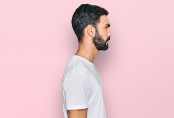 Wall Mural - Young hispanic man wearing casual white t shirt looking to side, relax profile pose with natural face with confident smile.